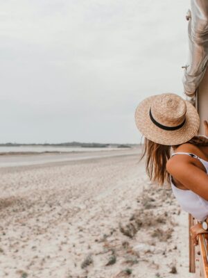 Woman in straw hat leans out of a train window, enjoying a beachside journey.
